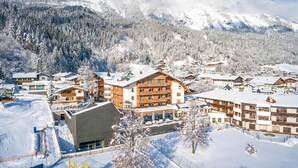 A snow-covered mountain resort with multiple buildings, including a prominent hotel with balconies and a ski slope in the foreground. - Hotel Schwarzbrunn Superior (Stans)