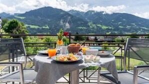 A table set for breakfast with a mountain view, including a basket of bread, a bowl of fruit, and a vase with flowers. - Hotel Schwarzbrunn Superior (Stans)