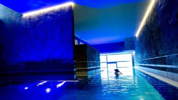 Una piscina interior con iluminación azul, una persona en el agua y vistas al área de la piscina.