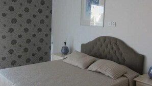 A bedroom with a large bed, a headboard, a nightstand, and a wall-mounted picture. - Bayview Gardens (Limassol)