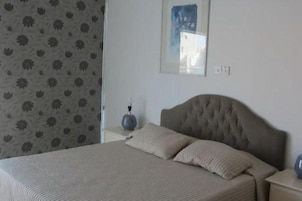 Un dormitorio con una cama grande, cabecera, mesita de noche y un cuadro en la pared.