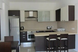A modern kitchen with dark cabinets, a stainless steel refrigerator, a built-in oven, and a large island with bar stools.