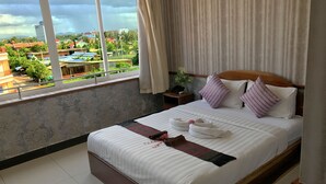 A hotel room with a large bed, a nightstand, a window with a view of the city, and a curtain. - Holiday Hotel (Battambang)
