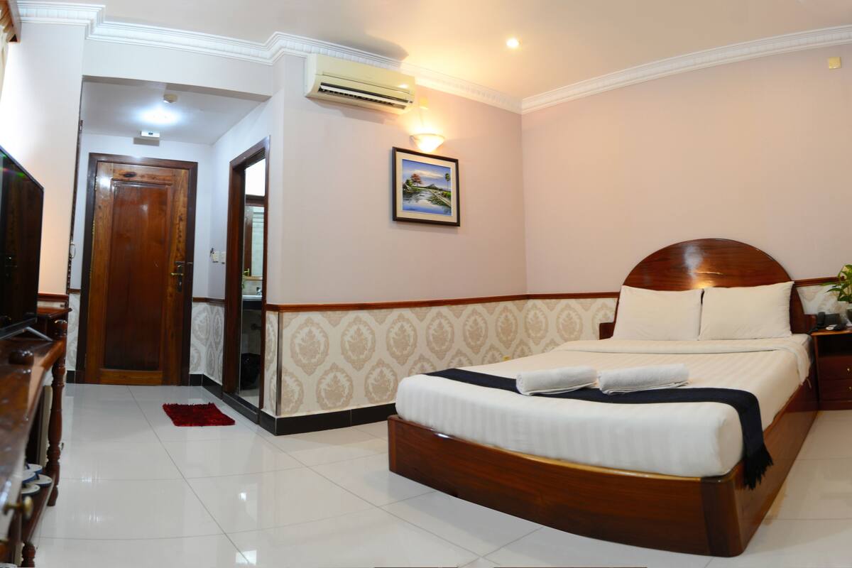 A hotel room with a wooden bed, a television, a red rug, and a framed picture on the wall.