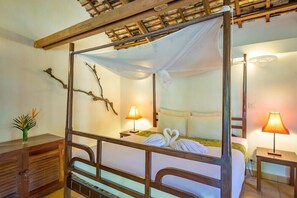 Un lit à baldaquin, une table de chevet avec une lampe et une branche décorative accrochée au mur.