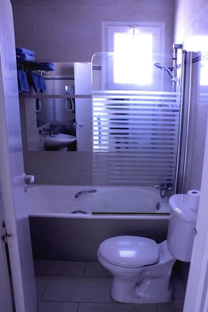 A compact bathroom with a toilet, a sink, and a shower area. - Paphinia Seaview Apartments (Paphos)