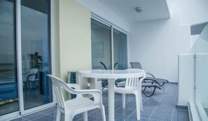 A modern room with a glass door leading to a balcony, a round table with chairs, and a ceiling light. - Paphinia Seaview Apartments (Paphos)