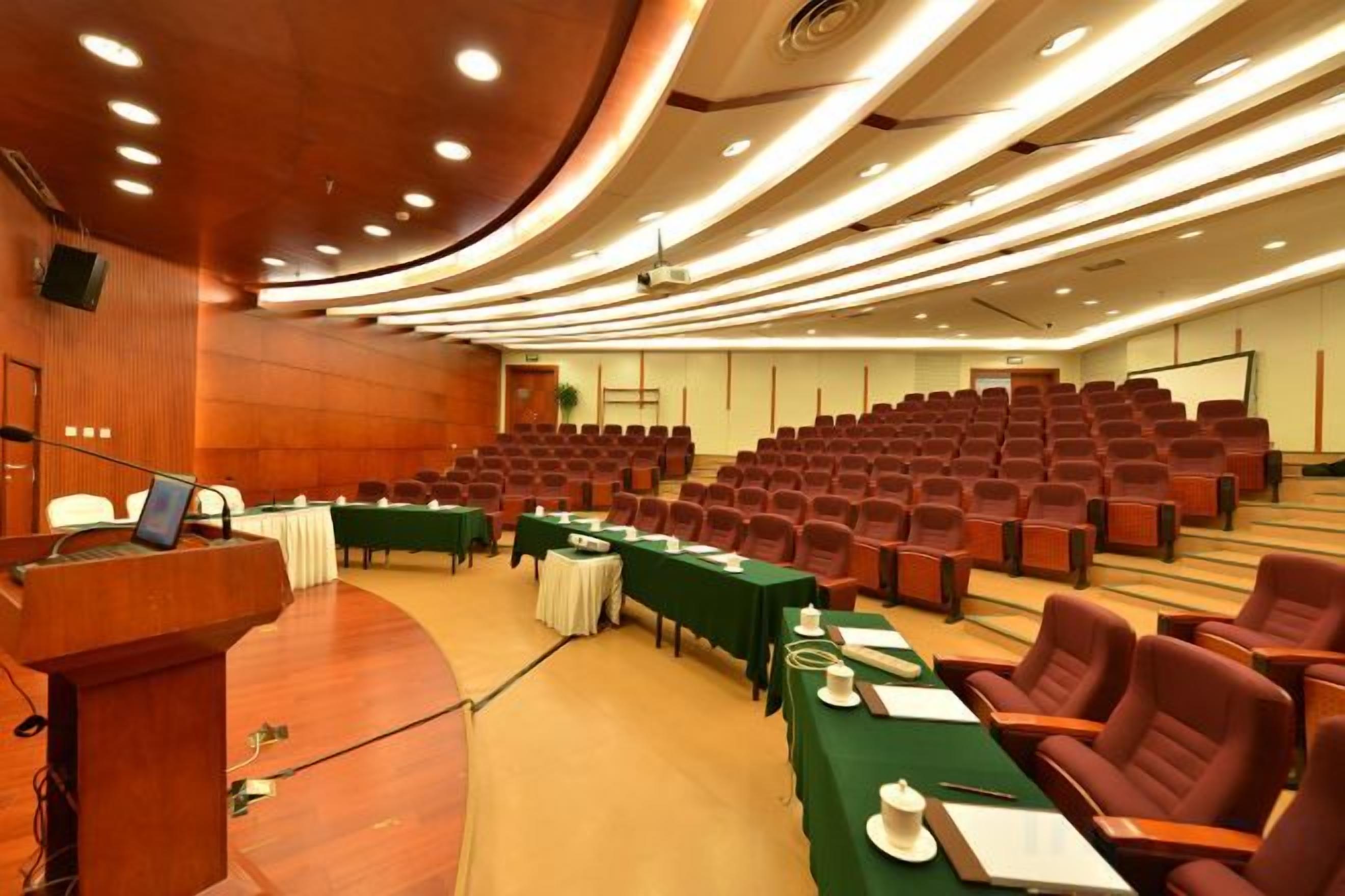 A conference room with a stage, multiple rows of chairs, and tables set up for a meeting.