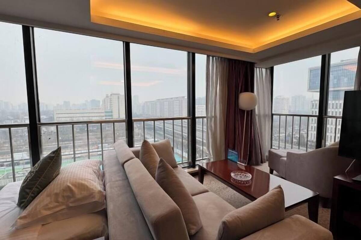 Une chambre d’hôtel moderne avec une grande fenêtre, un canapé, une télévision et une table.