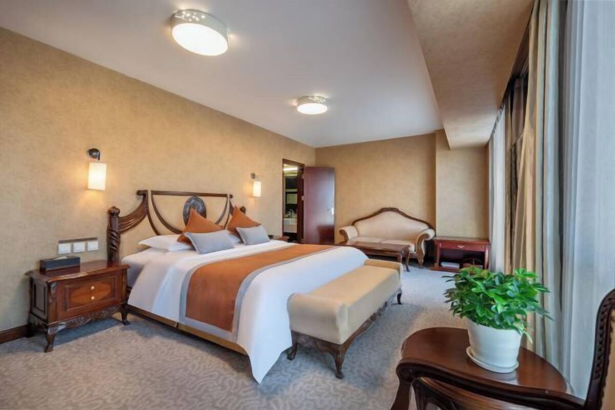 Une chambre d’hôtel avec un grand lit, des tables de chevet, une chaise, un bureau et une plante en pot.