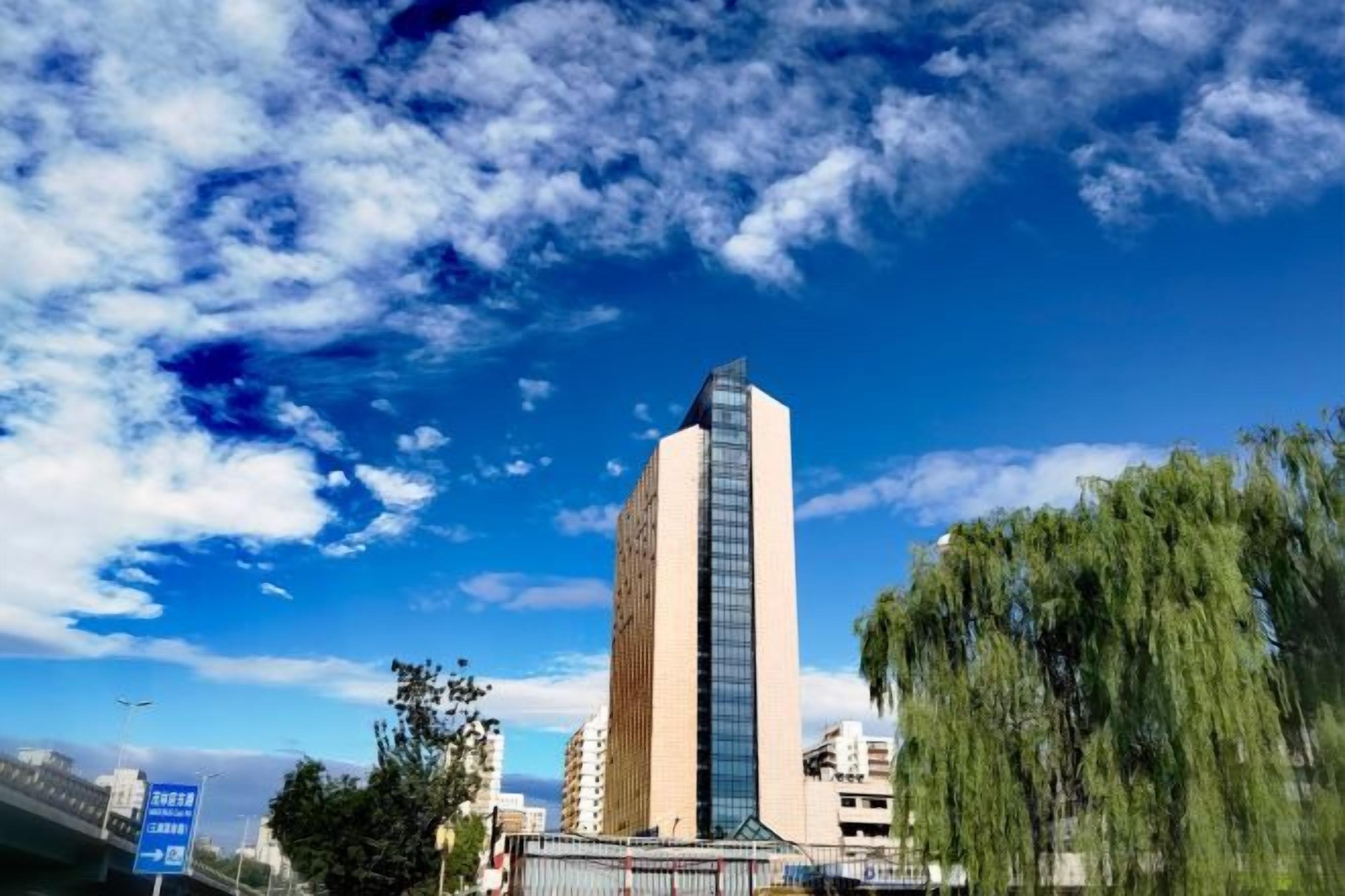 Un edificio alto de diseño moderno, rodeado de árboles bajo un cielo despejado.