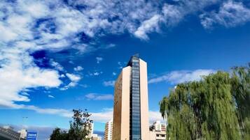 Un edificio alto de diseño moderno, rodeado de árboles bajo un cielo despejado.
