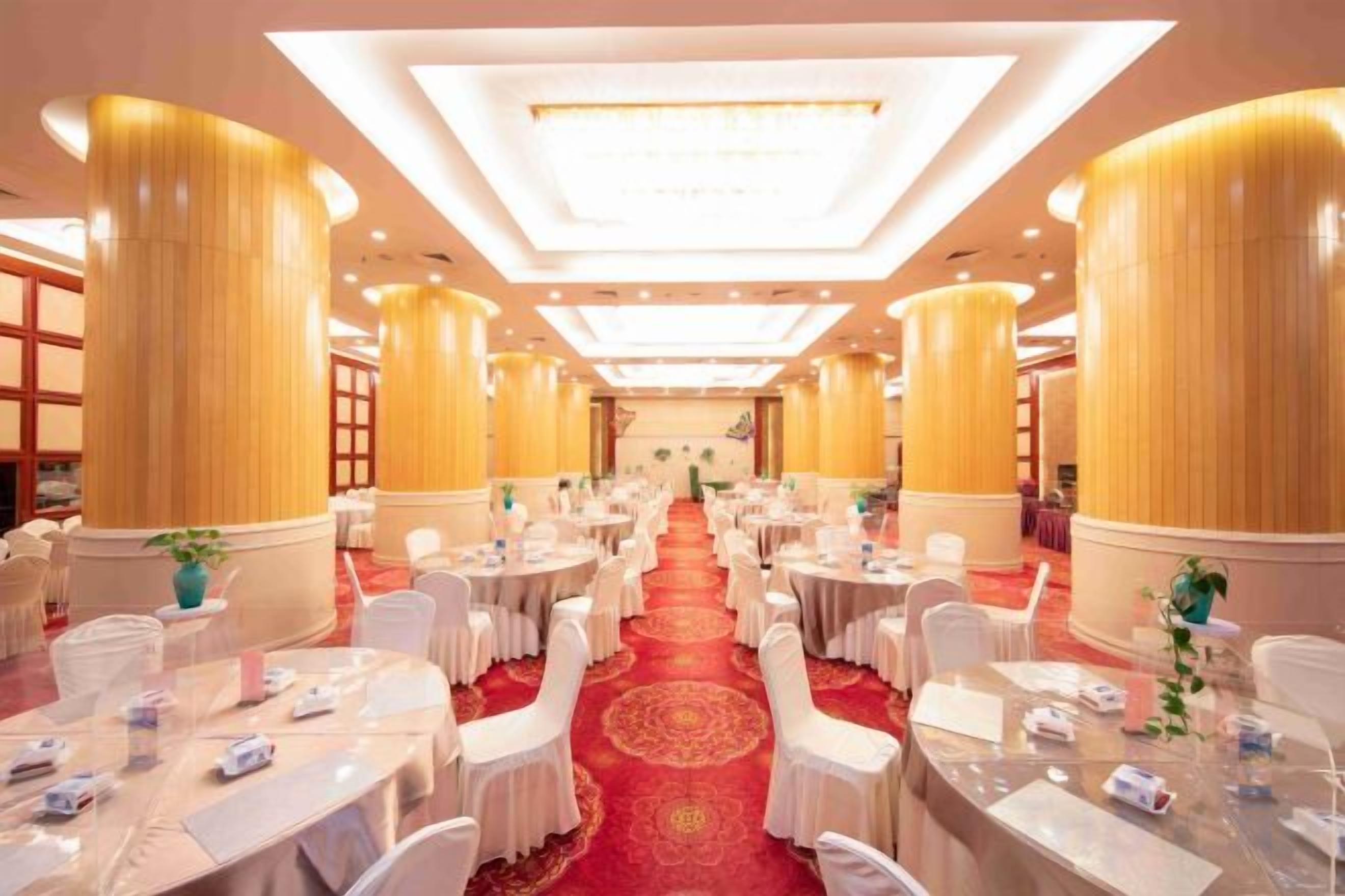 Un salón de banquetes con mesas redondas, sillas blancas y una alfombra roja.