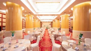 Un salón de banquetes con mesas redondas, sillas blancas y una alfombra roja.