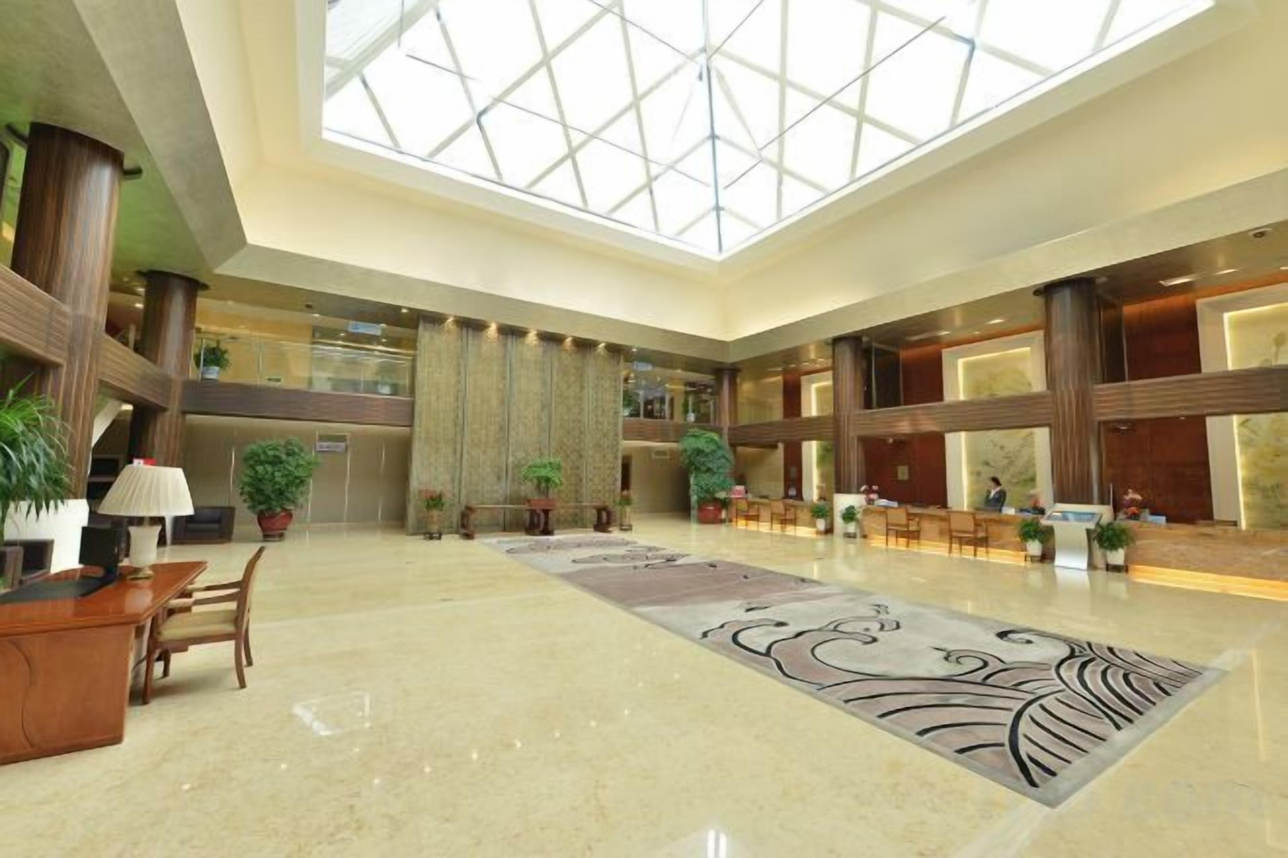 Een ruime lobby met een hoge plafond, een receptiebalie, zithoek en een groot raam.