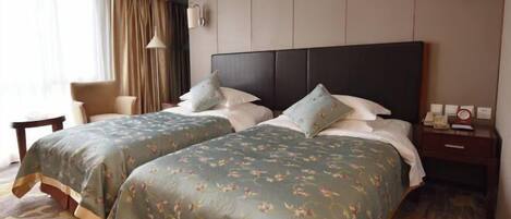 A hotel room with two beds, a chair, a nightstand, and a lamp.