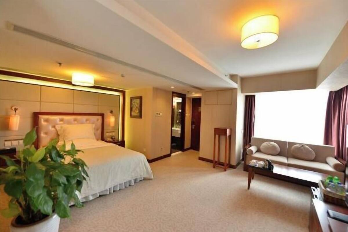 Une chambre d’hôtel avec un grand lit, un canapé, une petite table et une plante en pot.
