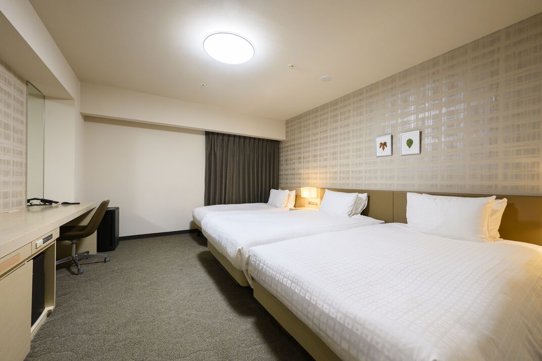 A hotel room with two beds, a desk, a chair, a desk lamp, and a mirror.