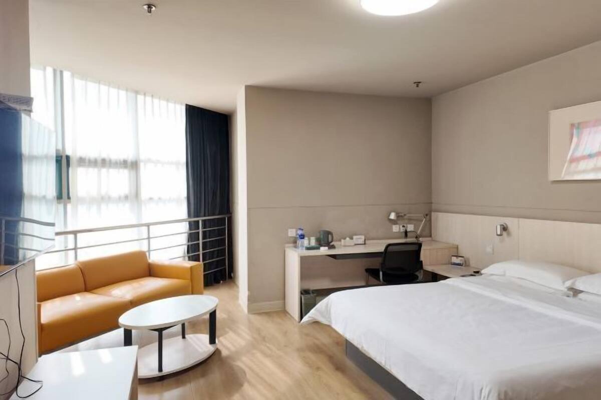 A hotel room with a bed, a desk, a chair, a sofa, and a TV.