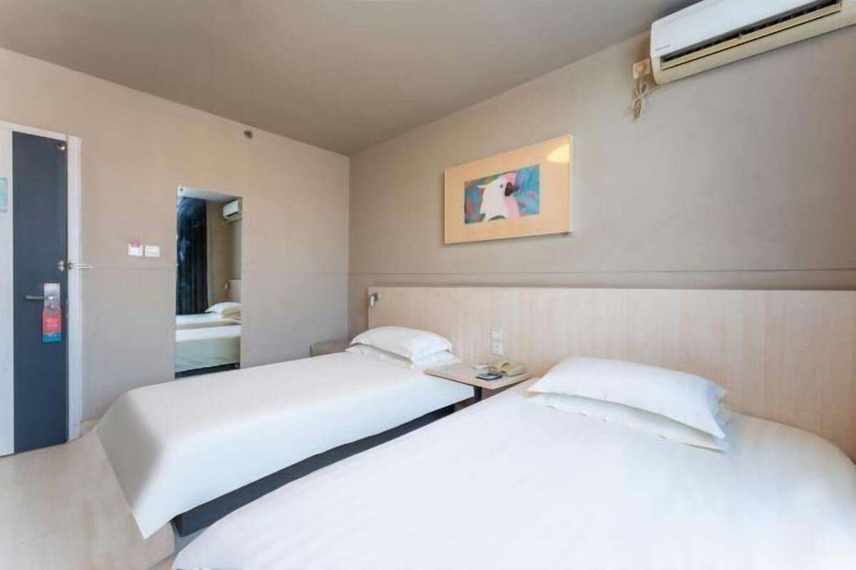 A hotel room with two beds, a door, an air conditioning unit, and a framed picture on the wall.
