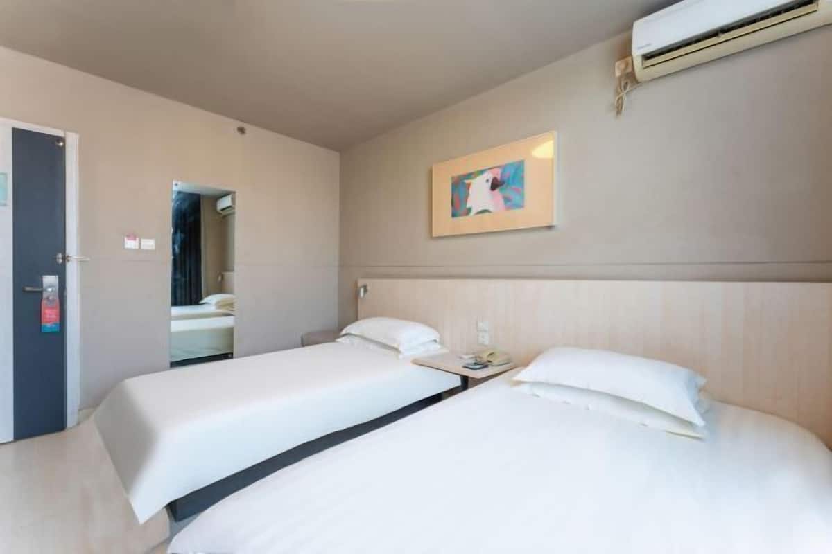 A hotel room with two beds, a door, an air conditioning unit, and a framed picture on the wall.