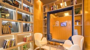 A modern hotel lobby with a wooden reception desk, two white armchairs, and a bookshelf filled with books and decorative items. - Jinjiang Inn (Huaibei Mengshan Road) (Huaibei)