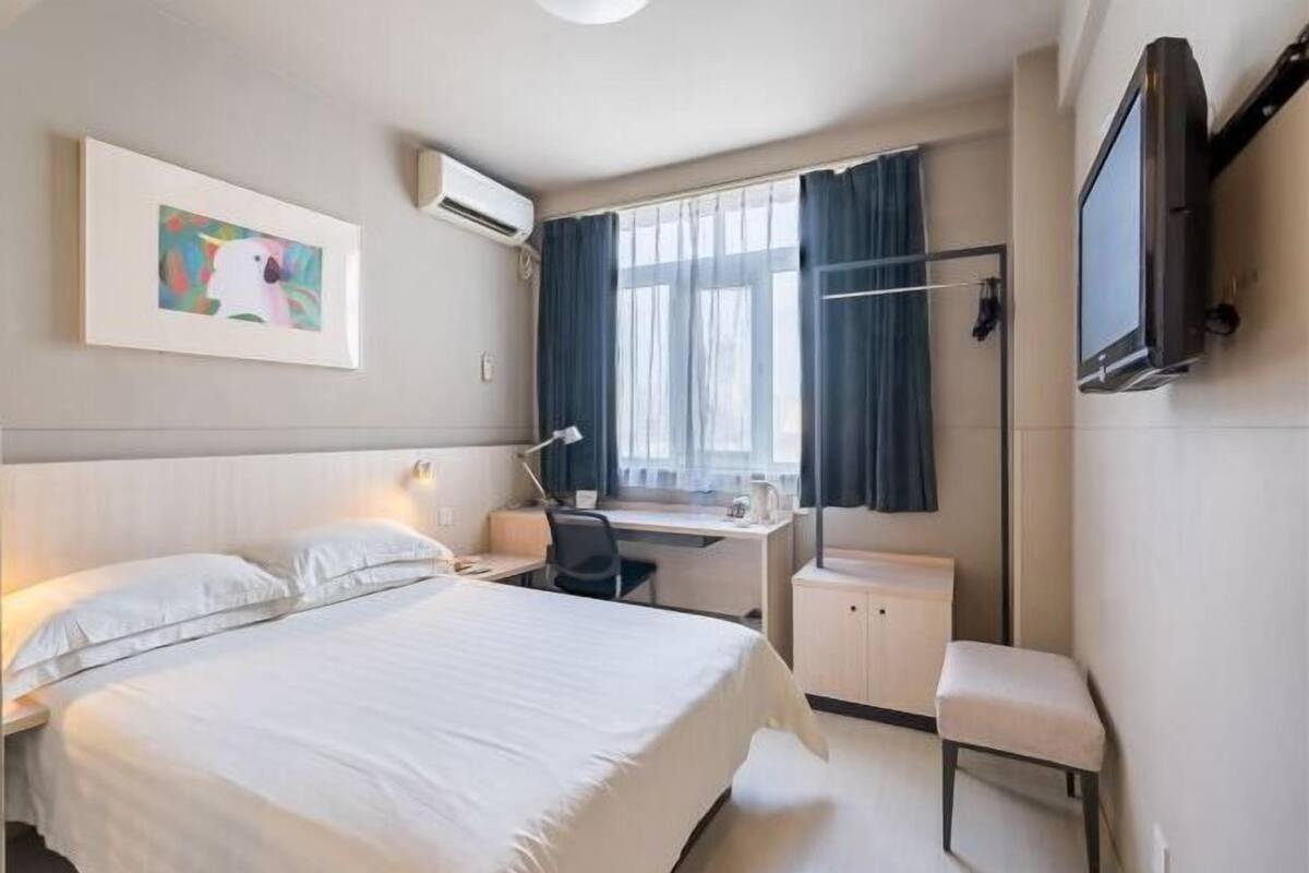 A hotel room with a bed, desk, chair, TV, and artwork.