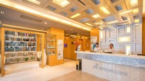 A reception area with a reception desk labeled "JINJIANG INN," a glass display case with various items, and a wooden shelving unit with books and decorative objects. - Jinjiang Inn (Huaibei Mengshan Road) (Huaibei)