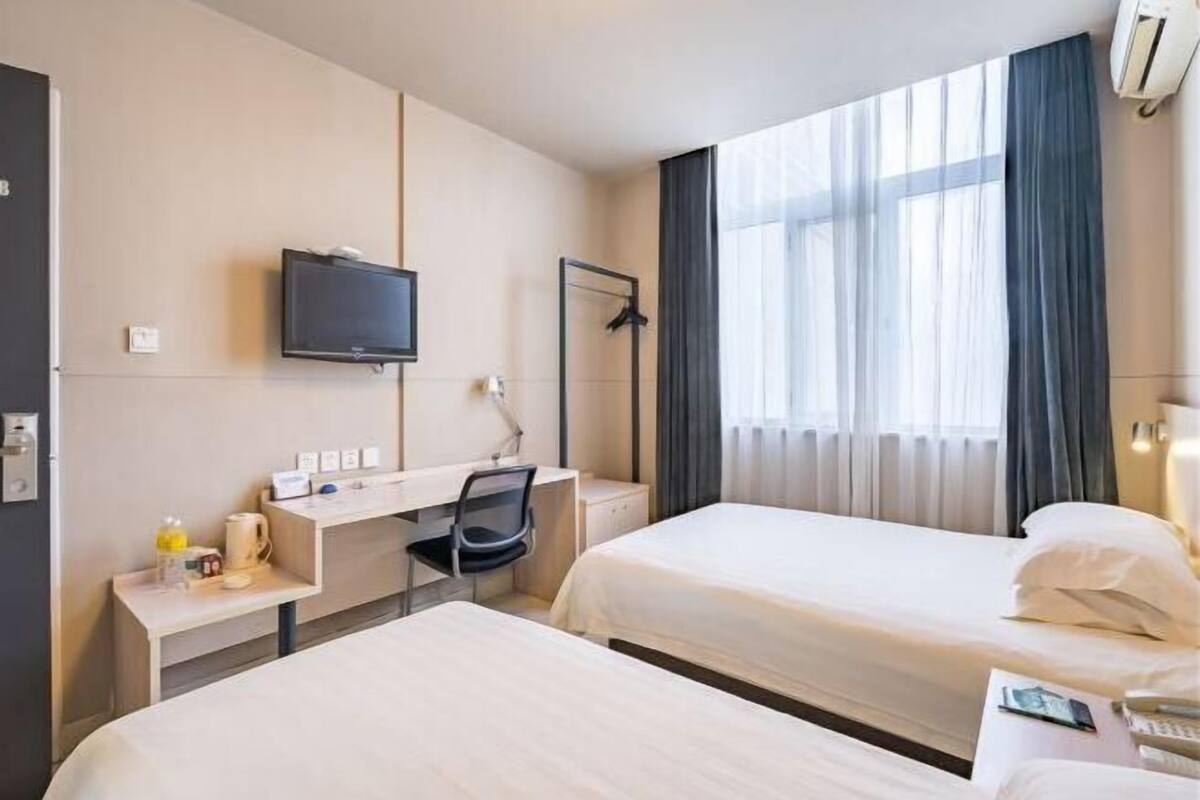 A hotel room with two beds, a desk with a chair, a television, and a window with curtains.