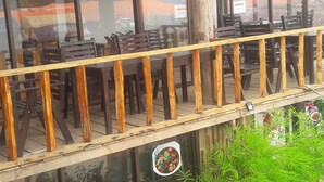 A restaurant with outdoor seating, wooden railings, and a view of the mountains through large windows.