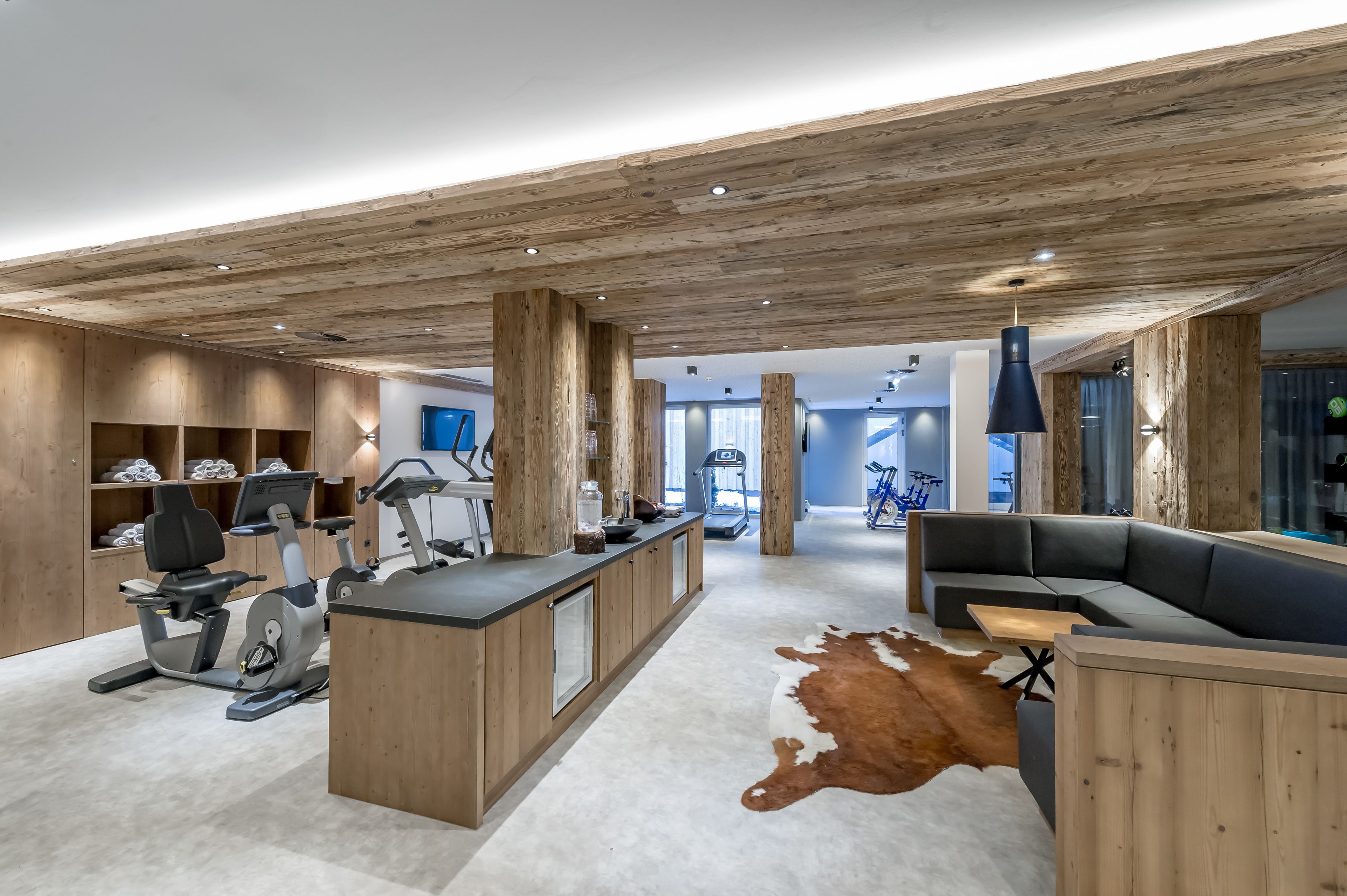 A modern interior with a wooden ceiling, a central island with exercise equipment, a seating area, and a glass wall.
