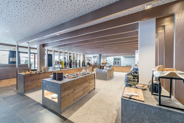 Un área de cocina moderna y amplia con una isla central, armarios de madera y una zona de estar con banco y mesa.