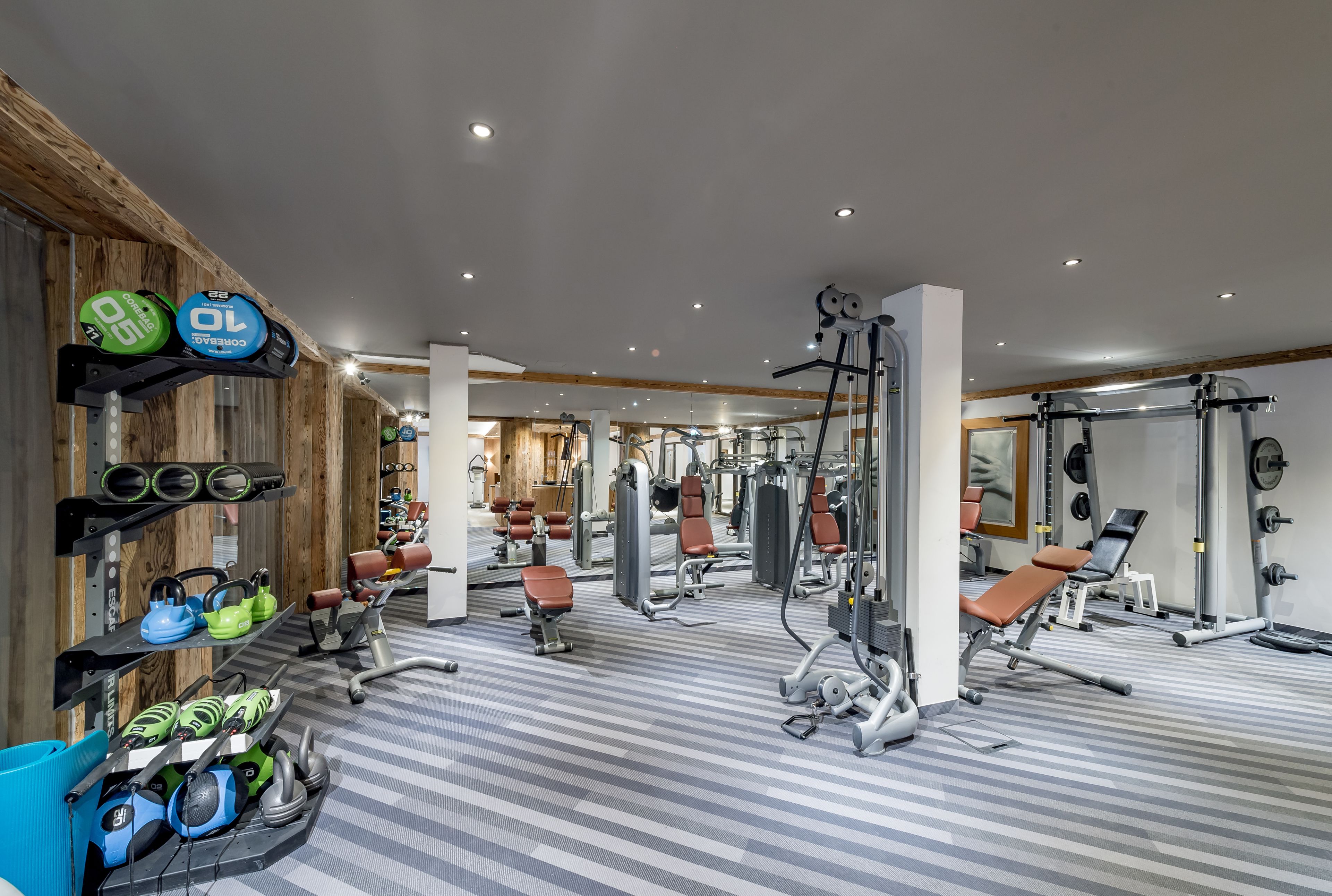 Un gimnasio con equipamiento de levantamiento de pesas, máquinas de ejercicio y un espejo grande.
