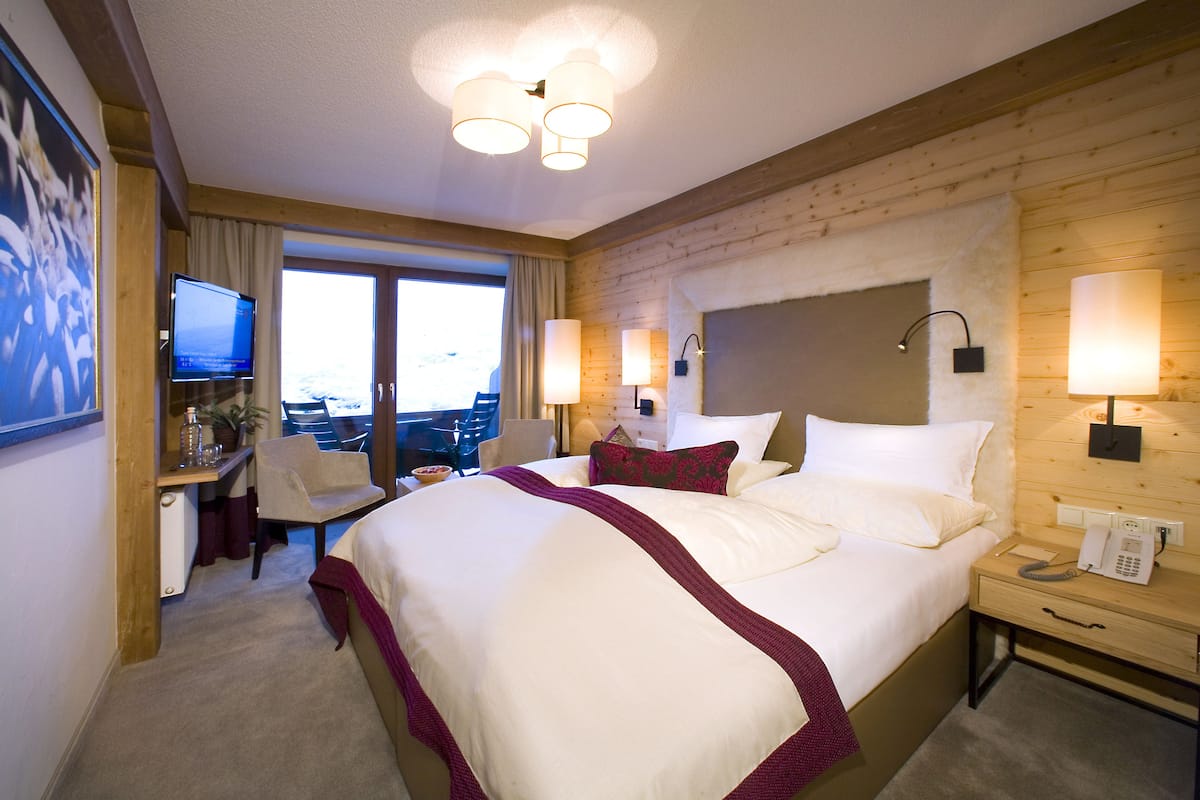A hotel room with a large bed, a desk with a chair, a television, and a view of the outdoors.