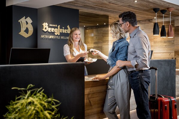 Un área de recepción con interior de madera, una pared negra con un logotipo y un mostrador de recepción.