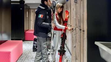 A locker room with wooden lockers, a red bench, and a person holding skis.
