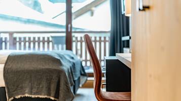 A room with a bed, a wooden chair, and a view of a balcony with a railing.