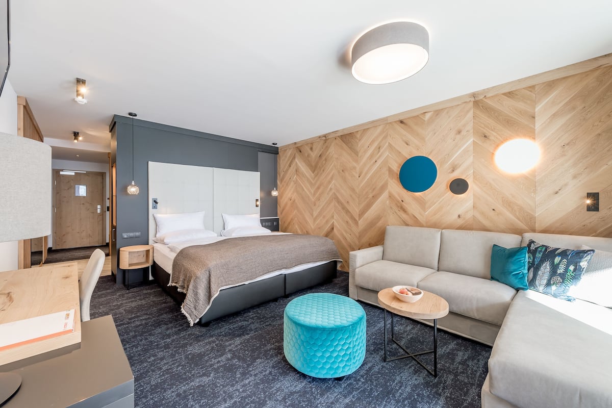 A modern hotel room with a bed, sofa, ottoman, and a small table.