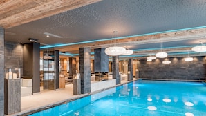 Ein moderner, überdachter Schwimmbereich mit blau gefliestem Boden, umgeben von steinernen Säulen und einer Holzbalkendecke.
