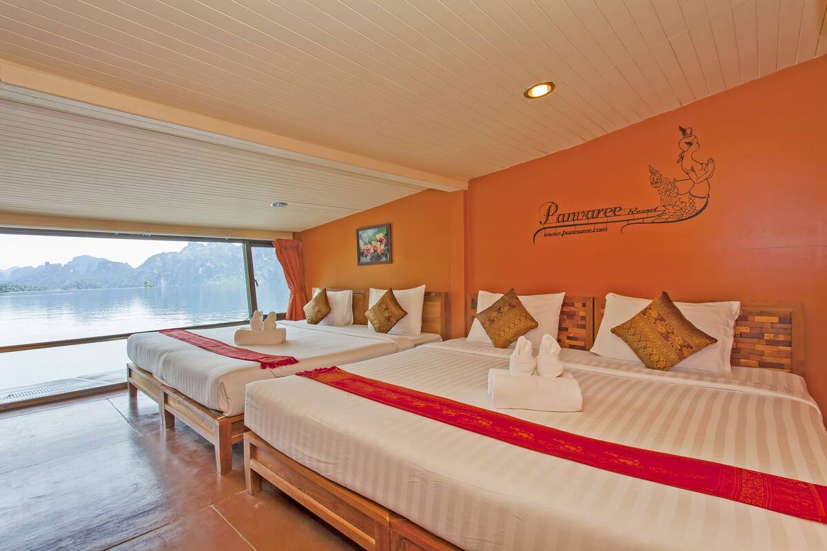 A hotel room with two beds, a large window with a view of the water, and a wall with a logo.