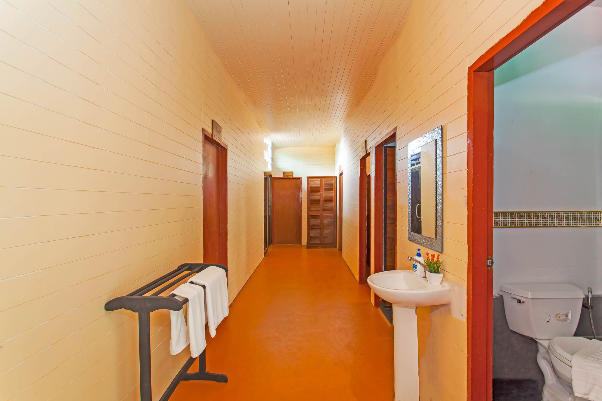 A hotel corridor with wooden walls, a bench with towels, a sink, and a toilet.