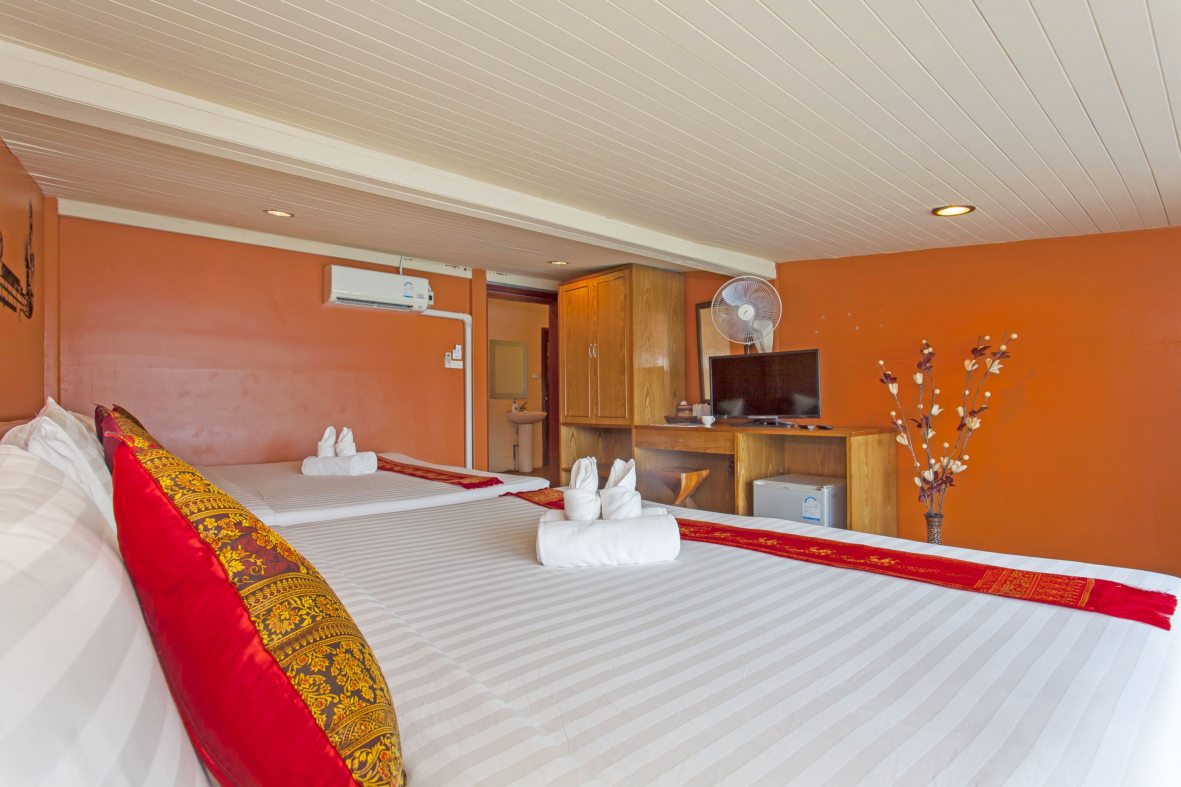 A hotel room with two beds, a TV, a desk, and a bathroom visible through an open door.