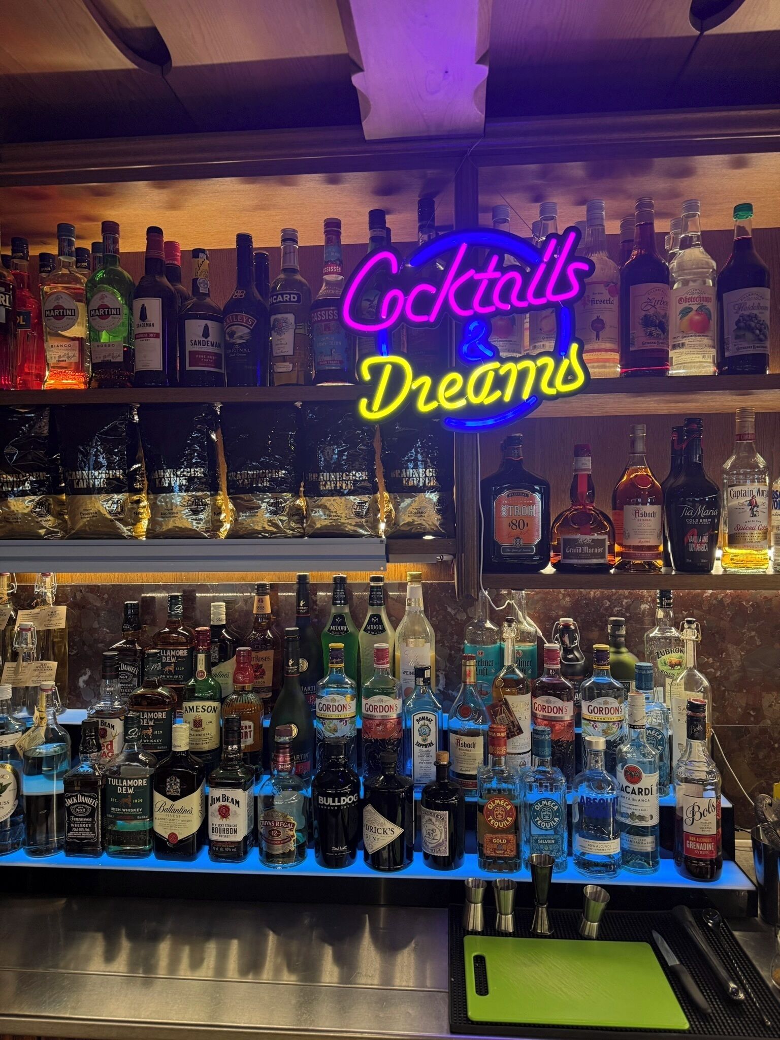 A bar with a neon sign reading "Cocktails Dreams" and a variety of liquor bottles.