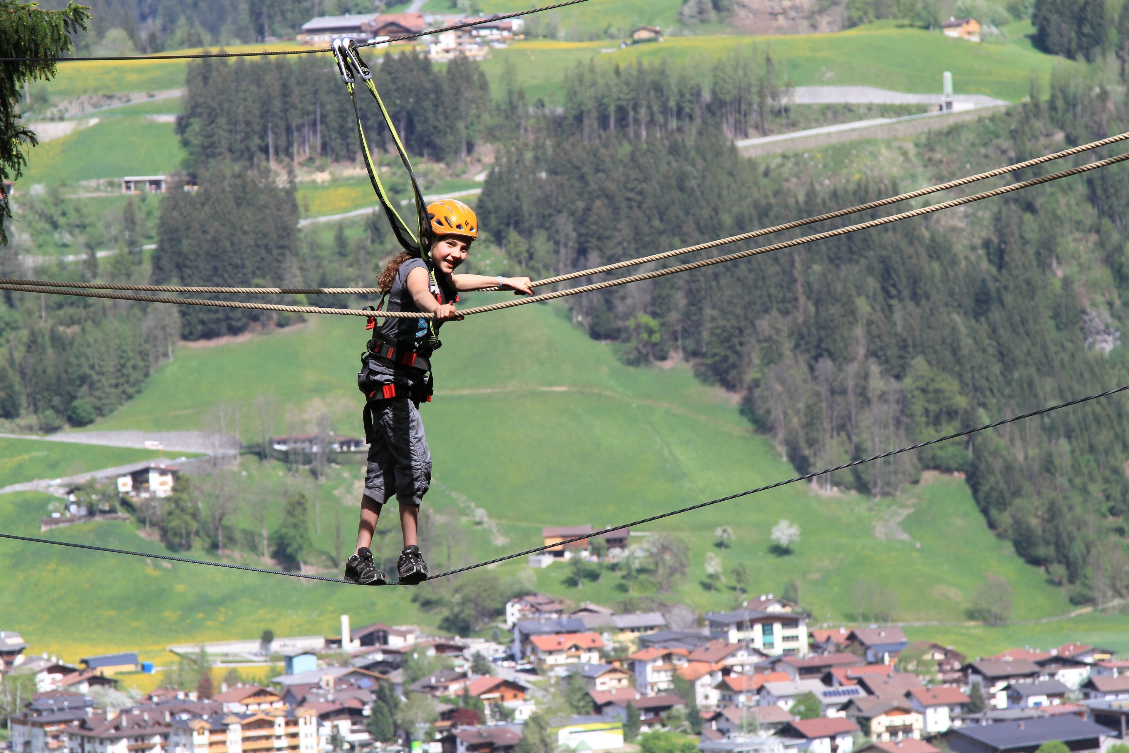 A person on a zip line with a mountainous landscape and a village below.