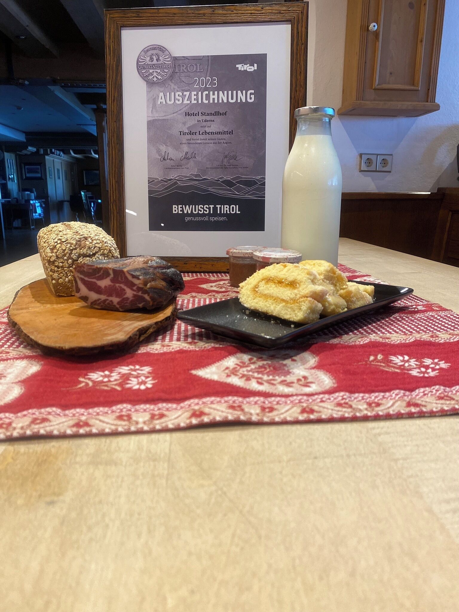 Ein gerahmtes Zertifikat auf einem Tisch, zusammen mit einem Brotlaib, Fleisch und einer Platte Gebäck.