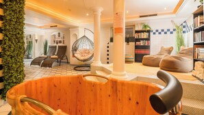 A wooden bathtub in a well-lit room with a checkered floor, a hanging chair, and a bookshelf. - Hotel Standlhof Zillertal (Uderns)