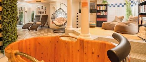 Una bañera de madera en una habitación bien iluminada con suelo a cuadros, un sillón colgante y una estantería.