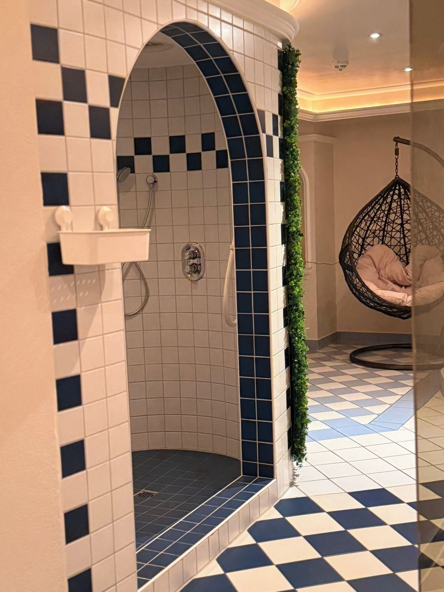 A bathroom with a checkered floor, a shower with a blue-tiled arch, and a hanging chair.