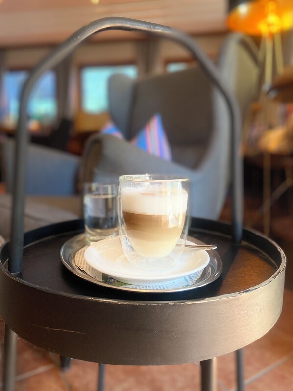 Una taza de café sobre una bandeja con un posavasos, colocada sobre una mesa en una habitación con un sofá y una lámpara al fondo.