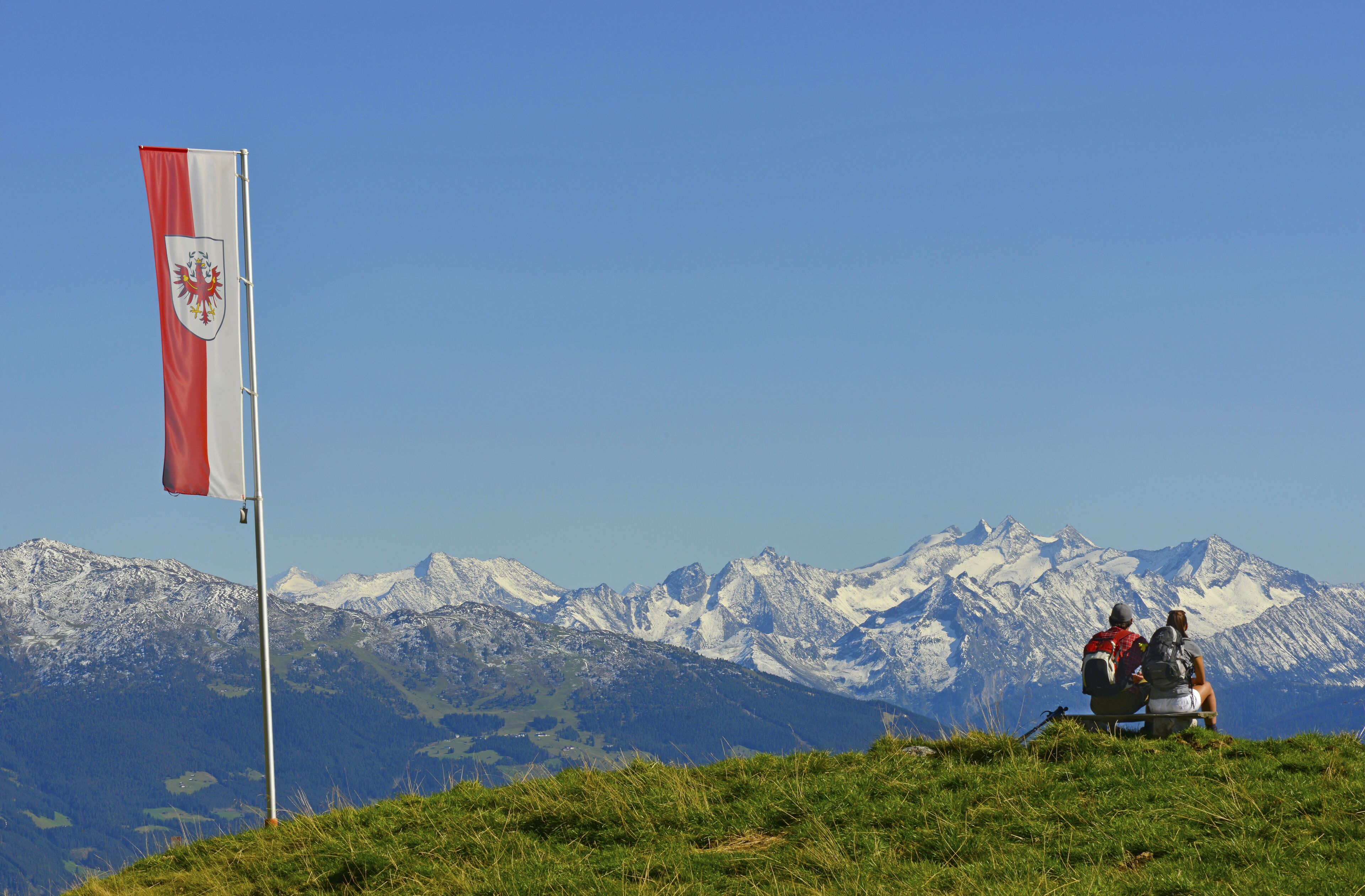 Un drapeau flottant au sommet d’un mât, avec une chaîne de montagnes en arrière-plan.